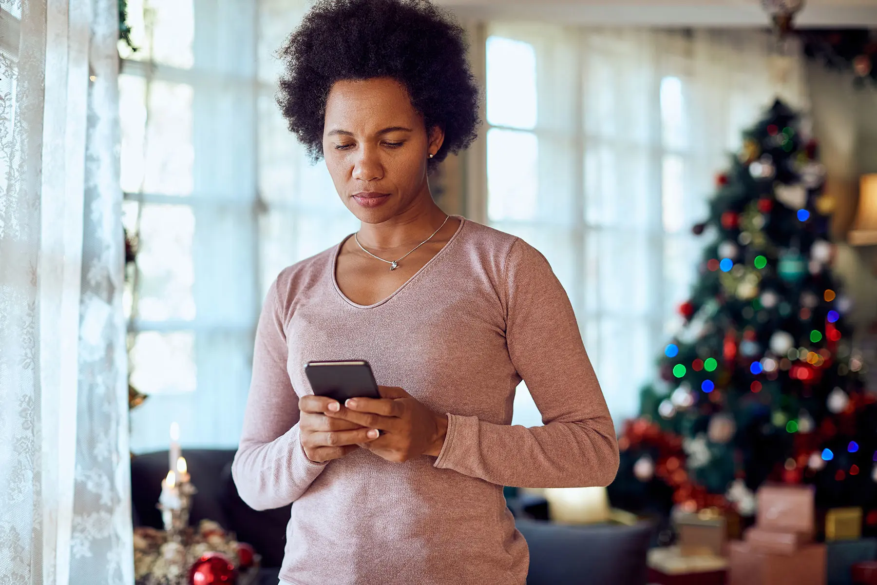 Black woman, serious, looking at phone with christmas tree in background. AW535