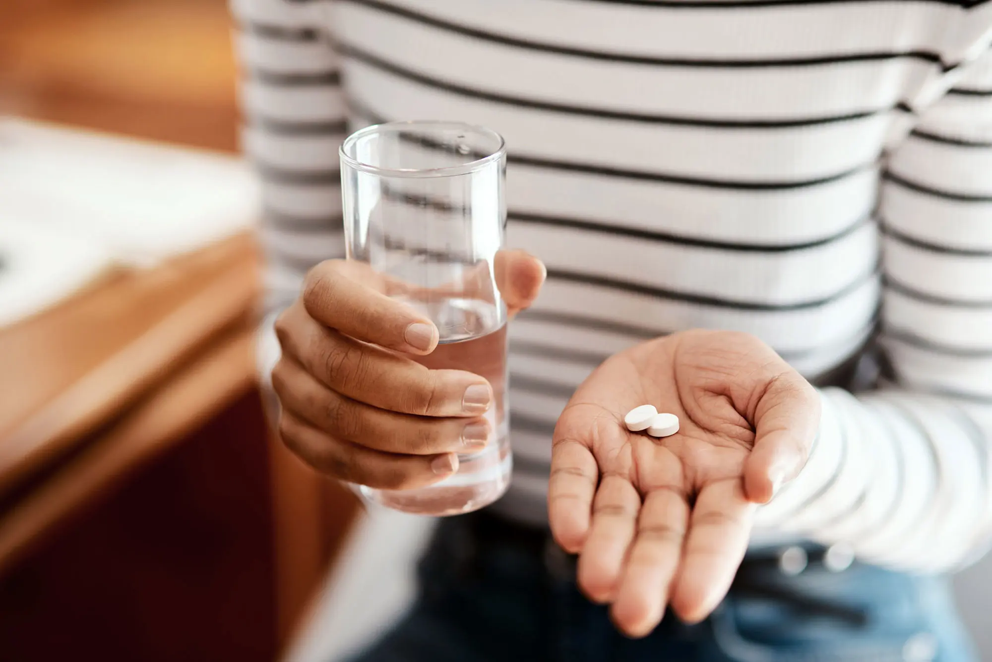Woman in striped shirt with glass of water and pills in the palm of her hand. AW477 