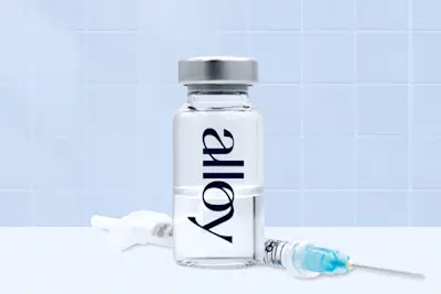 Alloy branded glass vial with syringe on white surface with blue tiled background - thumbnail