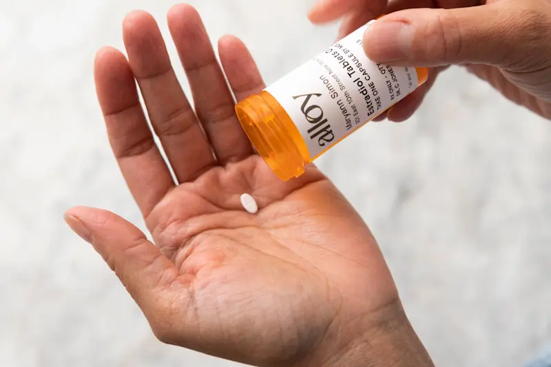 Woman with Estradiol pill in hand with Alloy branded Estradiol Tablets bottle.
