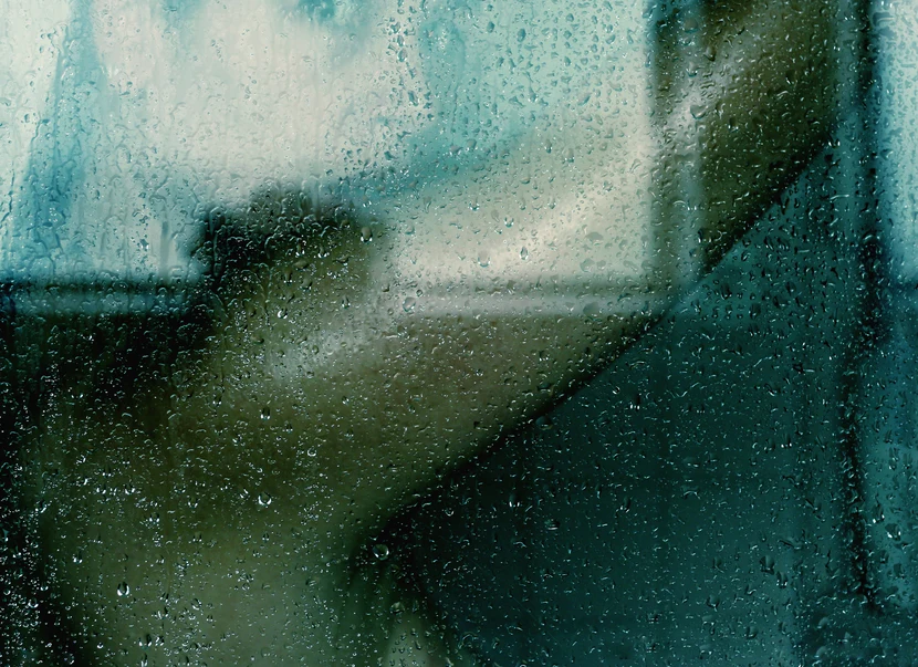 Woman taking cool shower, obscured by water droplets on glass. AW199