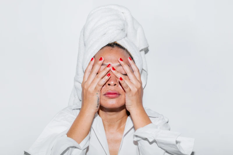 Blonde Asian Woman in bathrobe and towel turban with red painted nails covering face. AW181