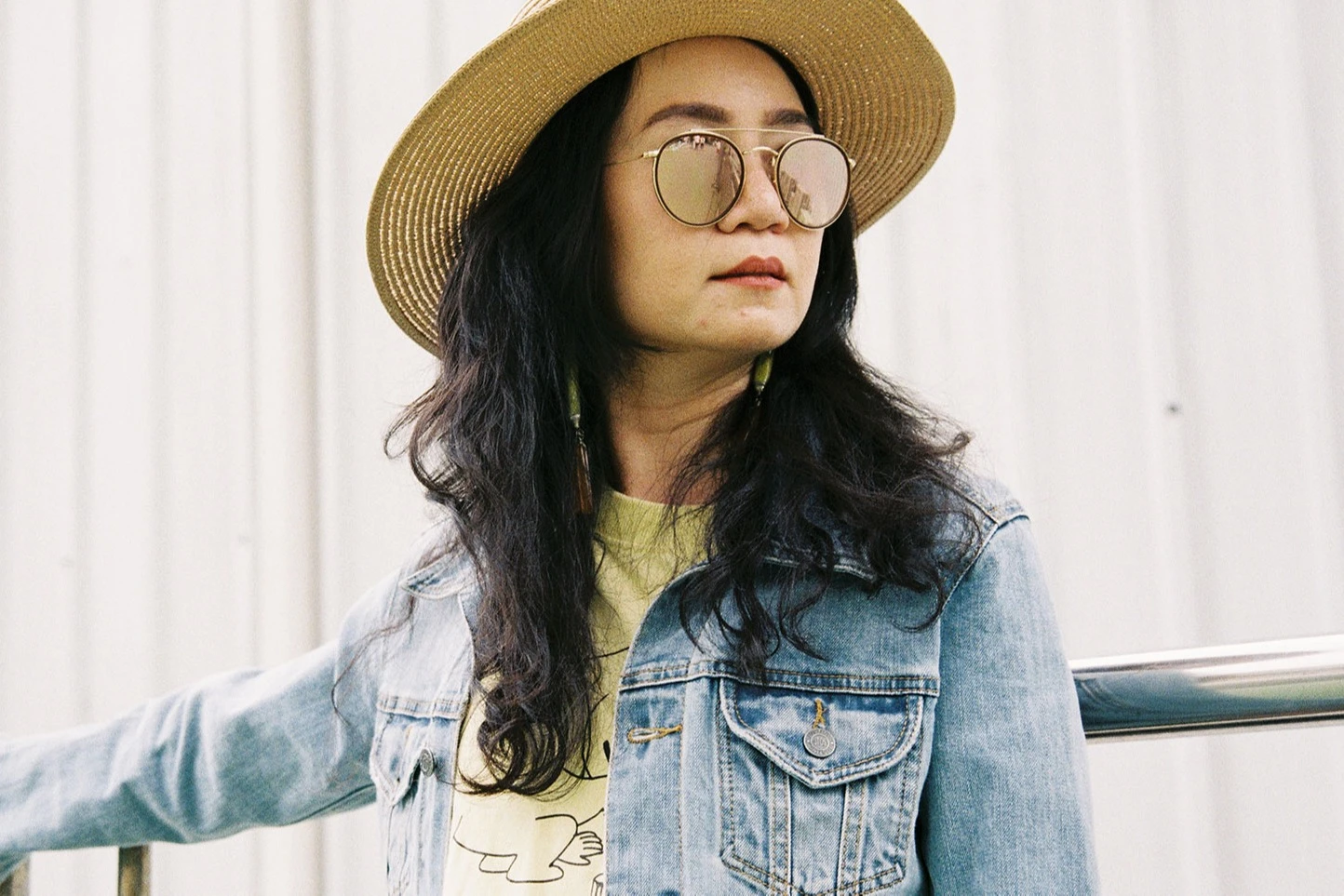 Asian woman in reflective sunglasses, denim jacket and straw hat looking away in thought. AW388