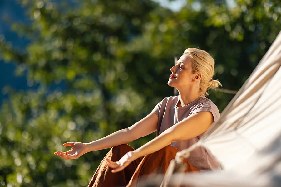 Blonde woman sitting outdoors with her eyes closed, palms up, breathing and taking in her environment (inline)