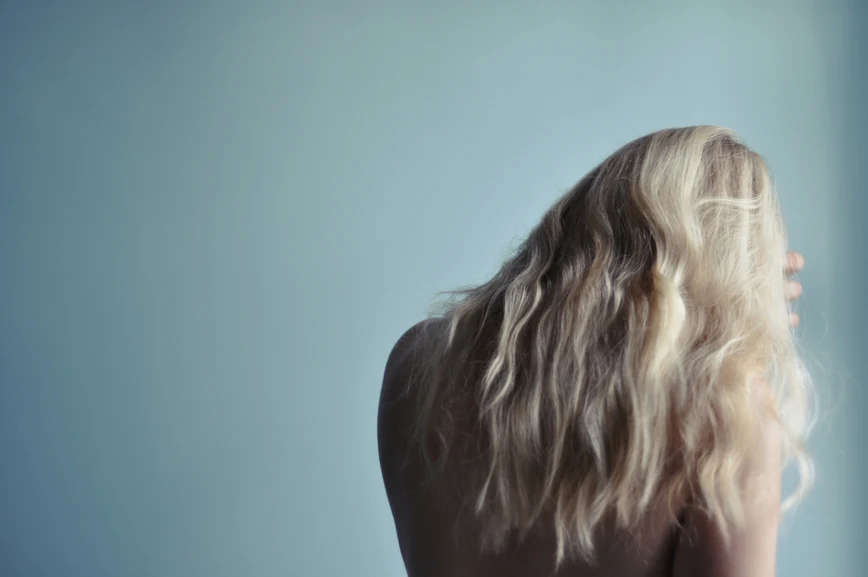 Rear view of a woman with long blond hair, bare shoulders, pulling hairs aside. AW122