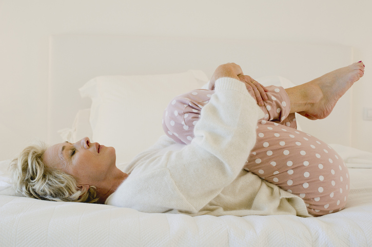AW282 Can Menopause Cause Insomnia? (photo showing mature blonde woman wearing pajamas in bed wrapping her arms around her legs)
