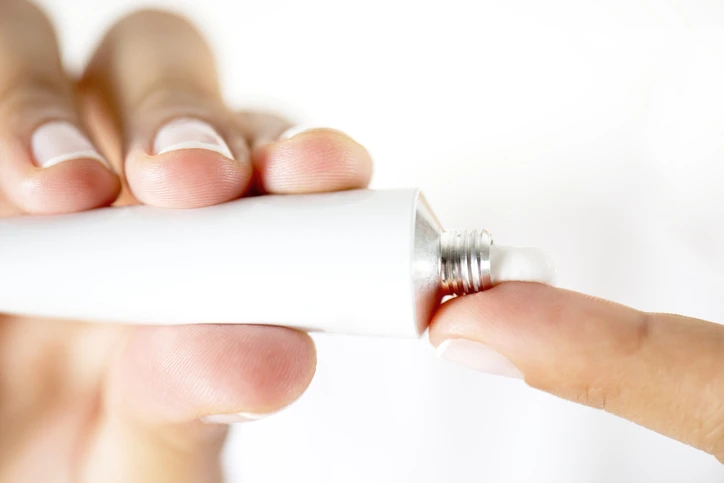 Womans hands holding tube of cream, applying to finger. AW074 