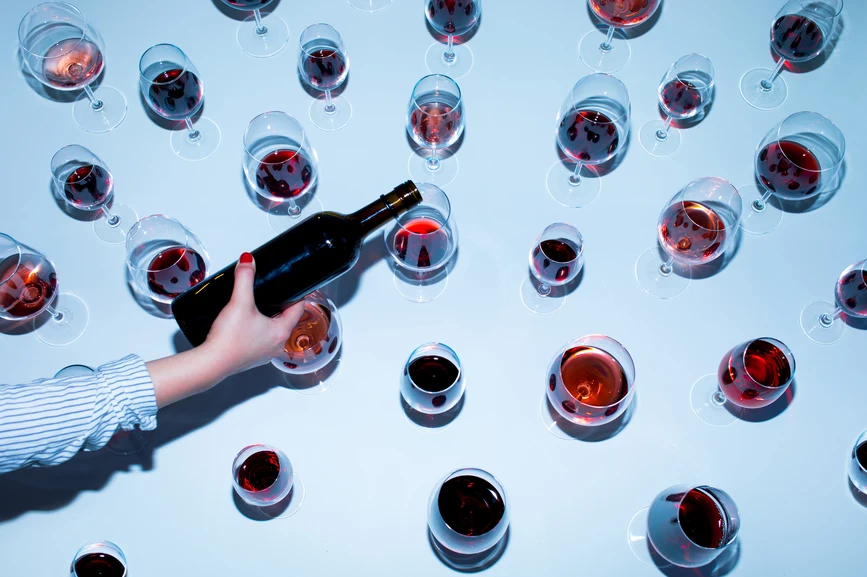 Overhead view - woman pouring red wine into multitude of glasses on blue background. AW093 