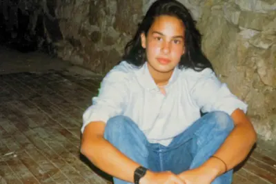  Monica Molenaar as a preteen sitting cross legged in jeans on rustic wood floor.
