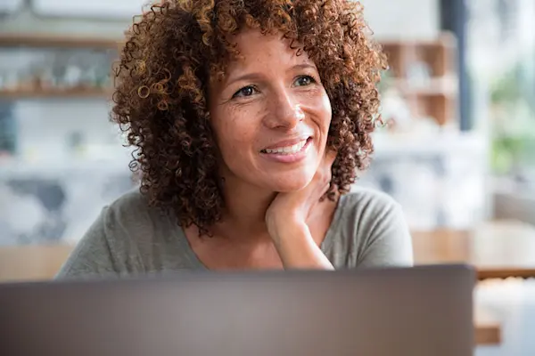 Biracial woman looking up from her laptop in coffee shop, smiling. AW485