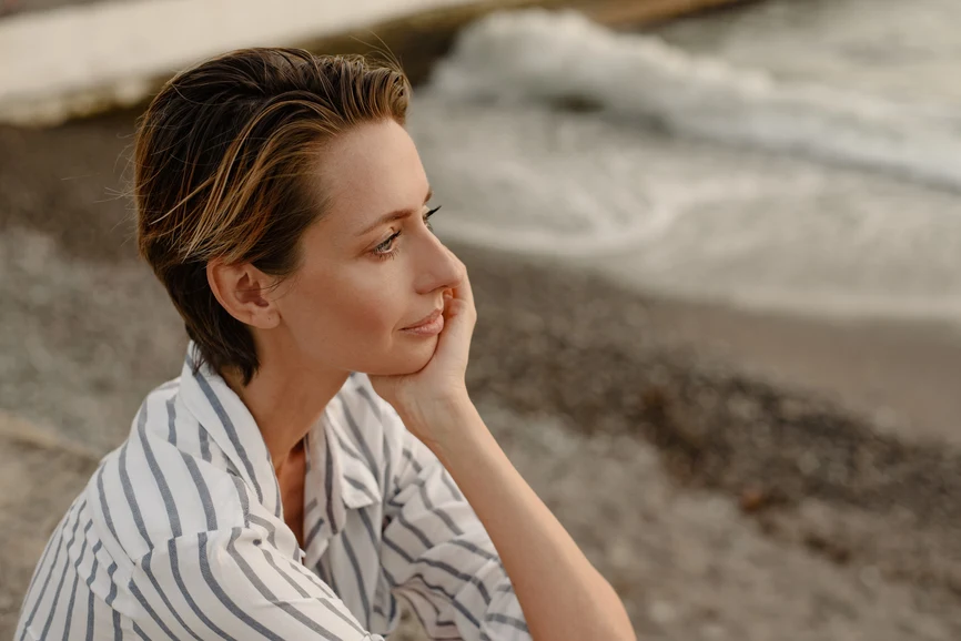 Woman resting hand on face at the shoreline. AW134