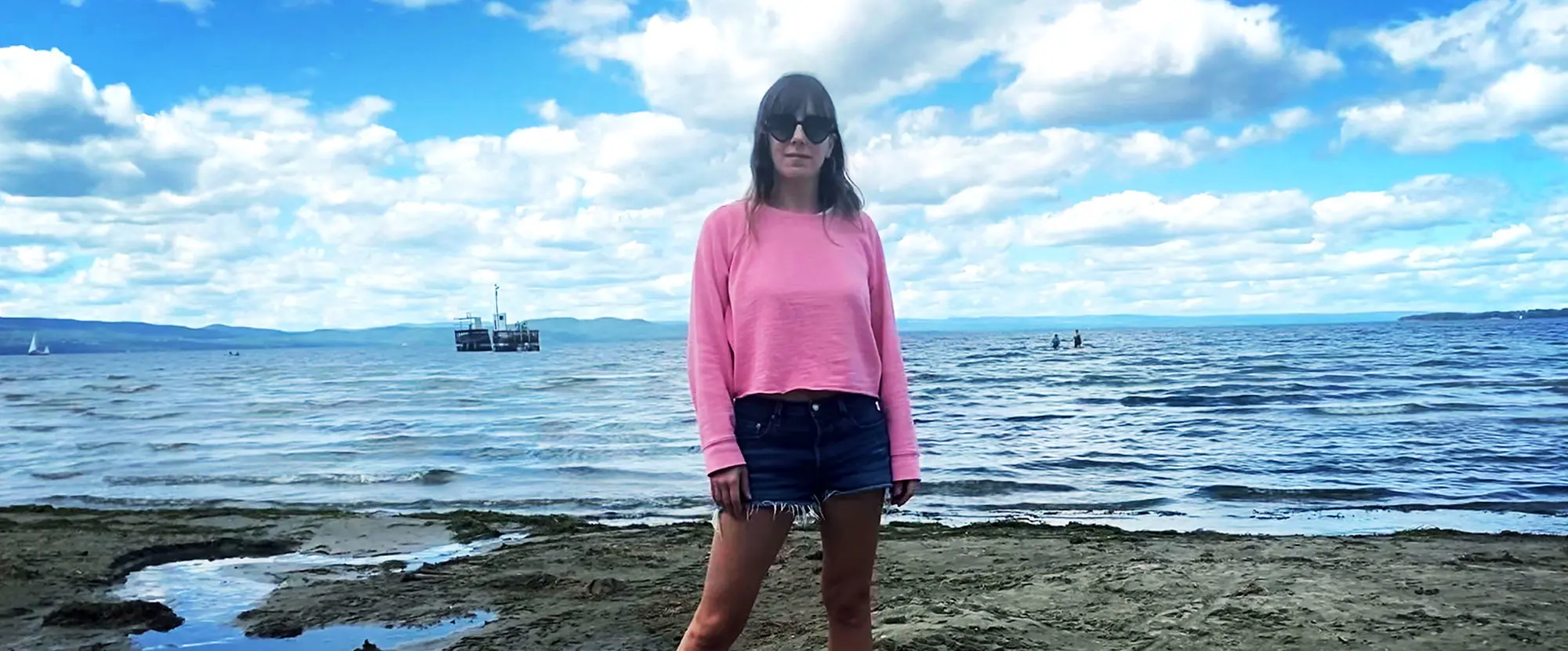 Lauren Waterman in pink sweatshirt and denim shorts in front of lake.