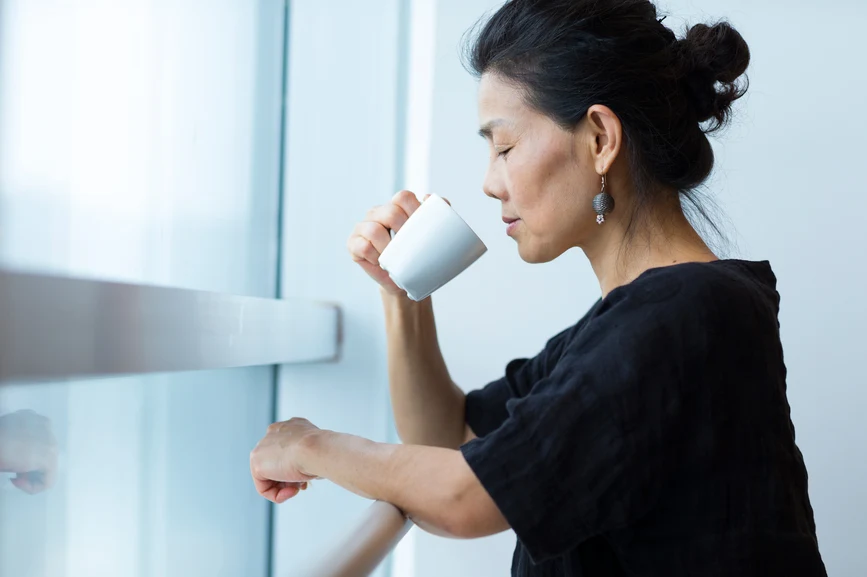 Asian woman resting at window drinking a warm beverage, eyes closed. AW131 