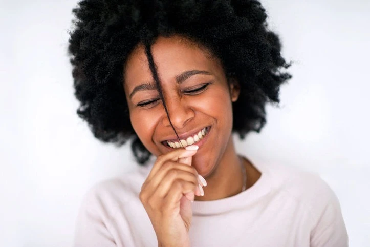 Black woman playfully pulling a curl in front of her face, smiling. AW237