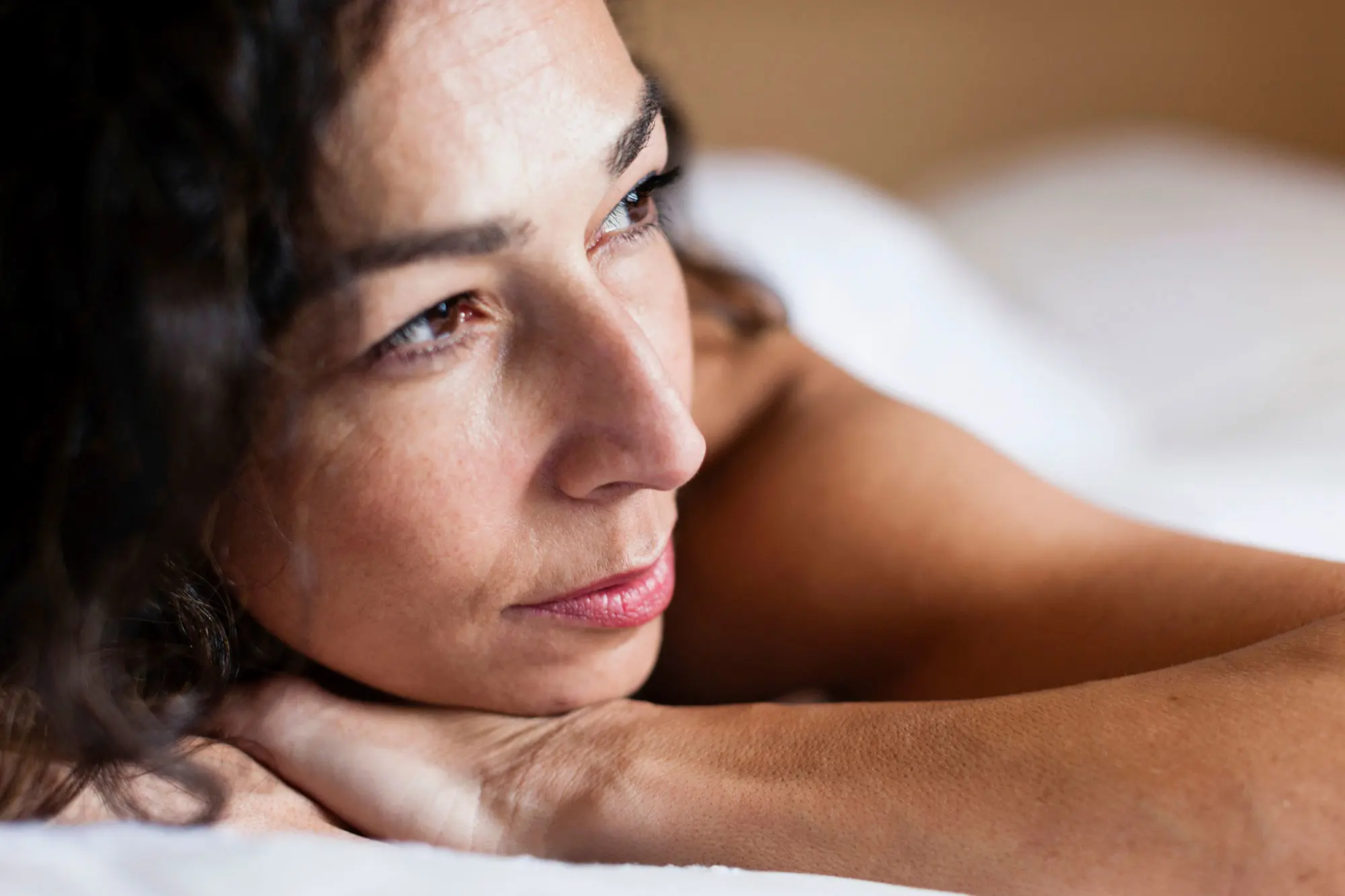 Woman in bed head resting on hands looking off into the distance. AW487