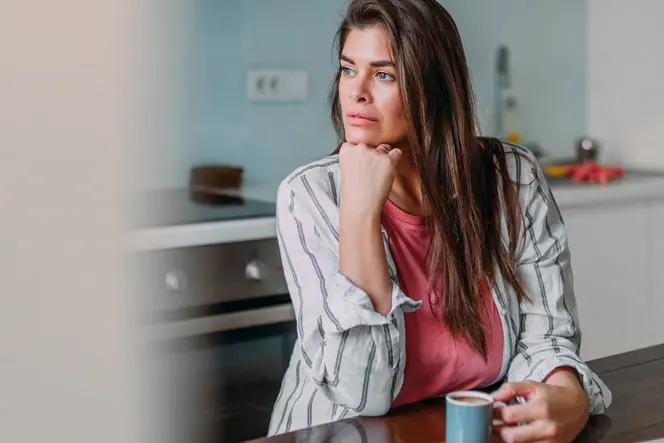 Woman looking off into distance while holding hot beverage in kitchen.  AW269