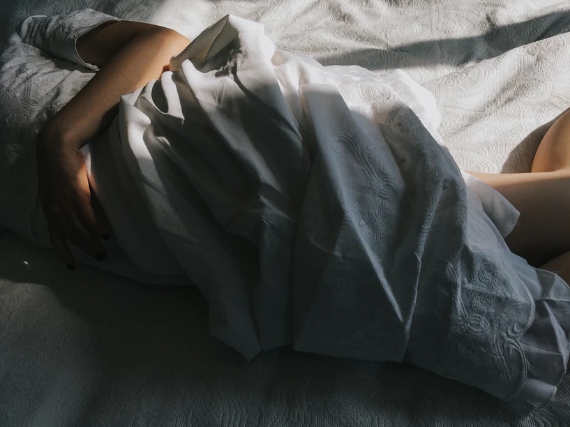 Woman in shadow wrapped in sheets on bed with sun coming through the windows. AW194