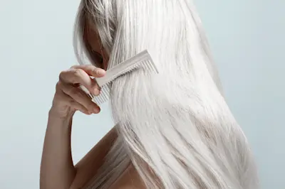 Woman combing long mane of platinum blonde or white hair, face obscured. AW163 
