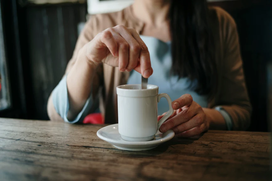 AW182 What is the Connection Between Hot Flashes and Headaches? (woman at table stirring cup of hot coffee)