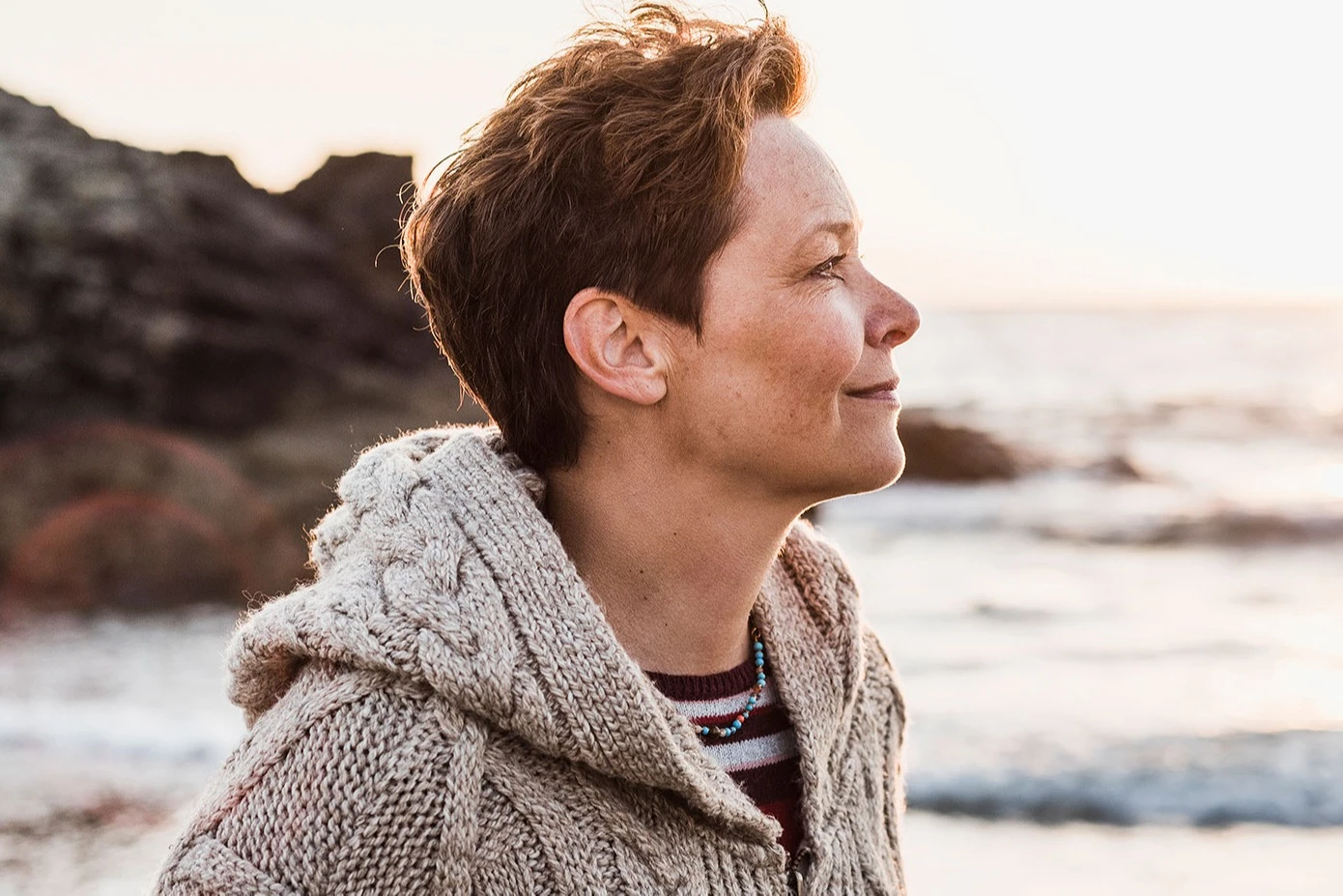 Woman with short hair at the beach lost in thought, smiling. AW470