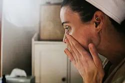 Middle aged woman rubbing serum into her skin while looking in a mirror. AW547 