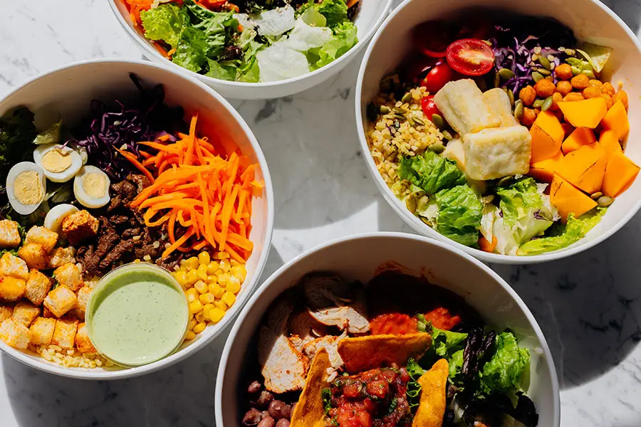 Four bowls of healthy meals including ingredients such as sweet potatoes, beans, eggs, broccoli, grains and vegetables photographed from above. inline
