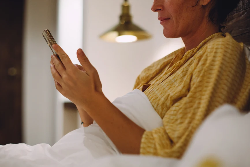 Woman in nightgown reading phone at night in bed with lights on. AW285