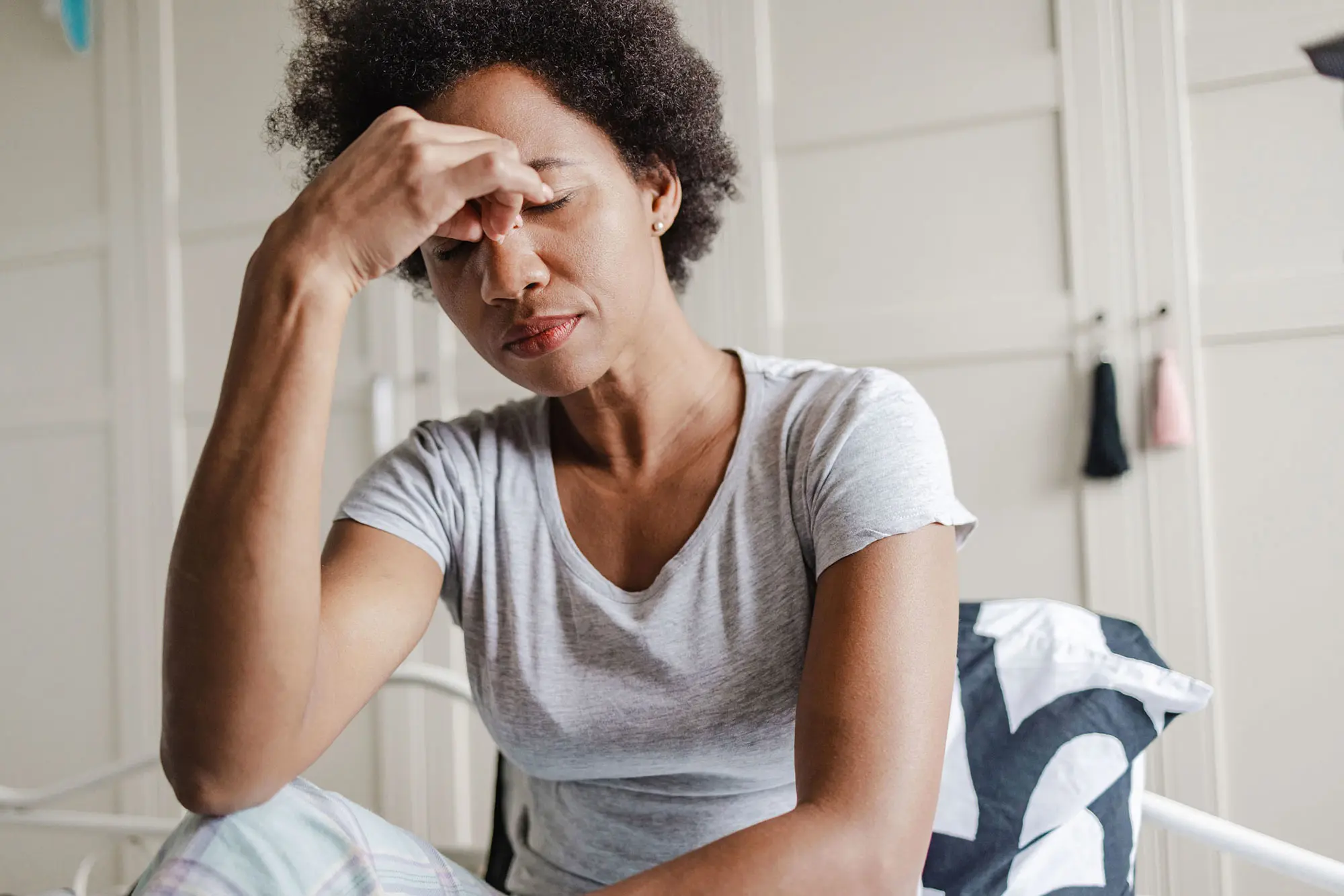 Biracial woman rubbing her eyes in bedroom daylight. AW457