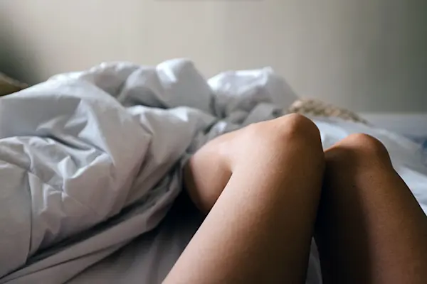 Womans bare legs in bed with rumpled sheets cast aside.  AW404