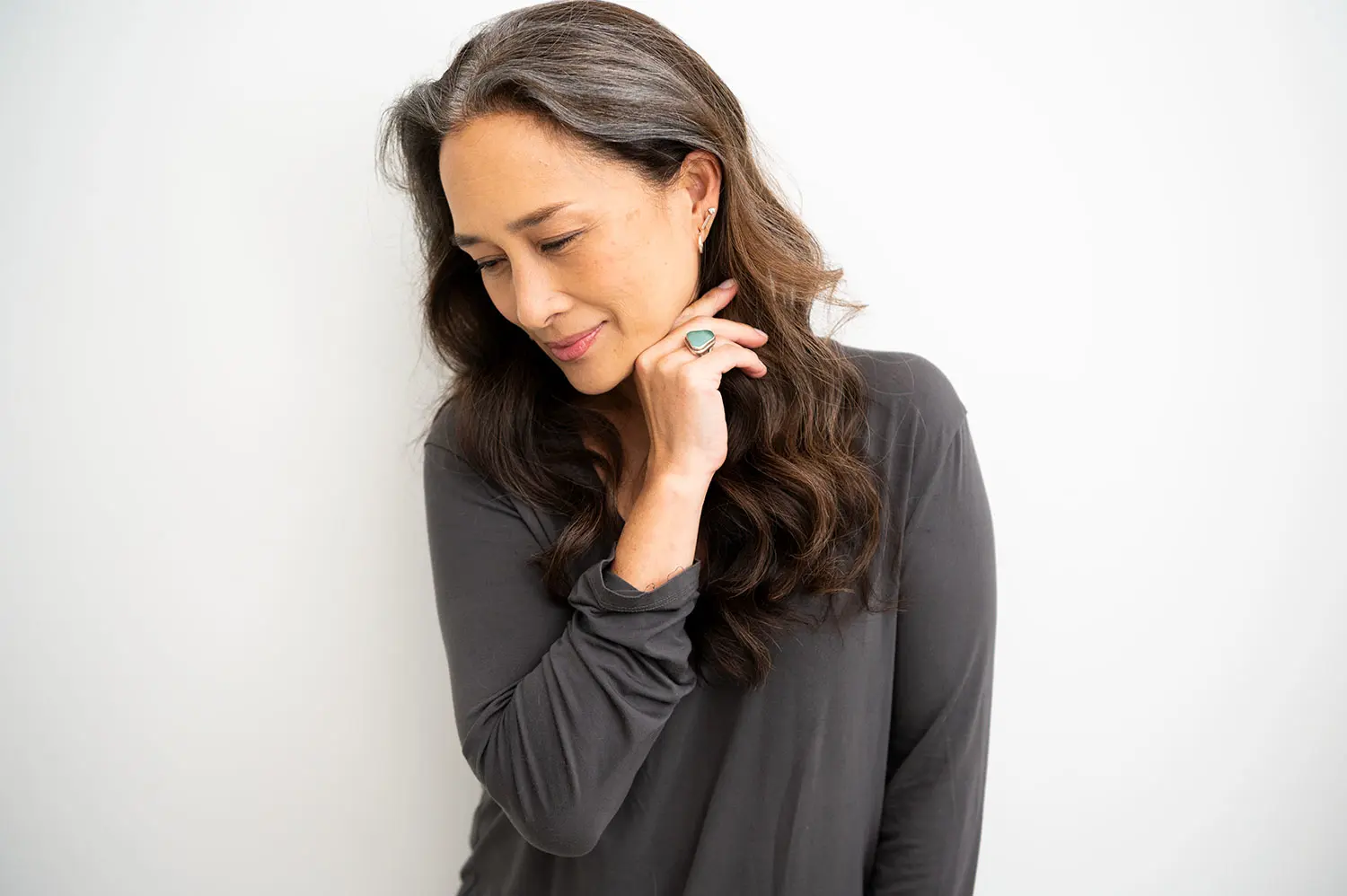 Woman of Asian descent with turquoise ring, holding back hair, looking down.