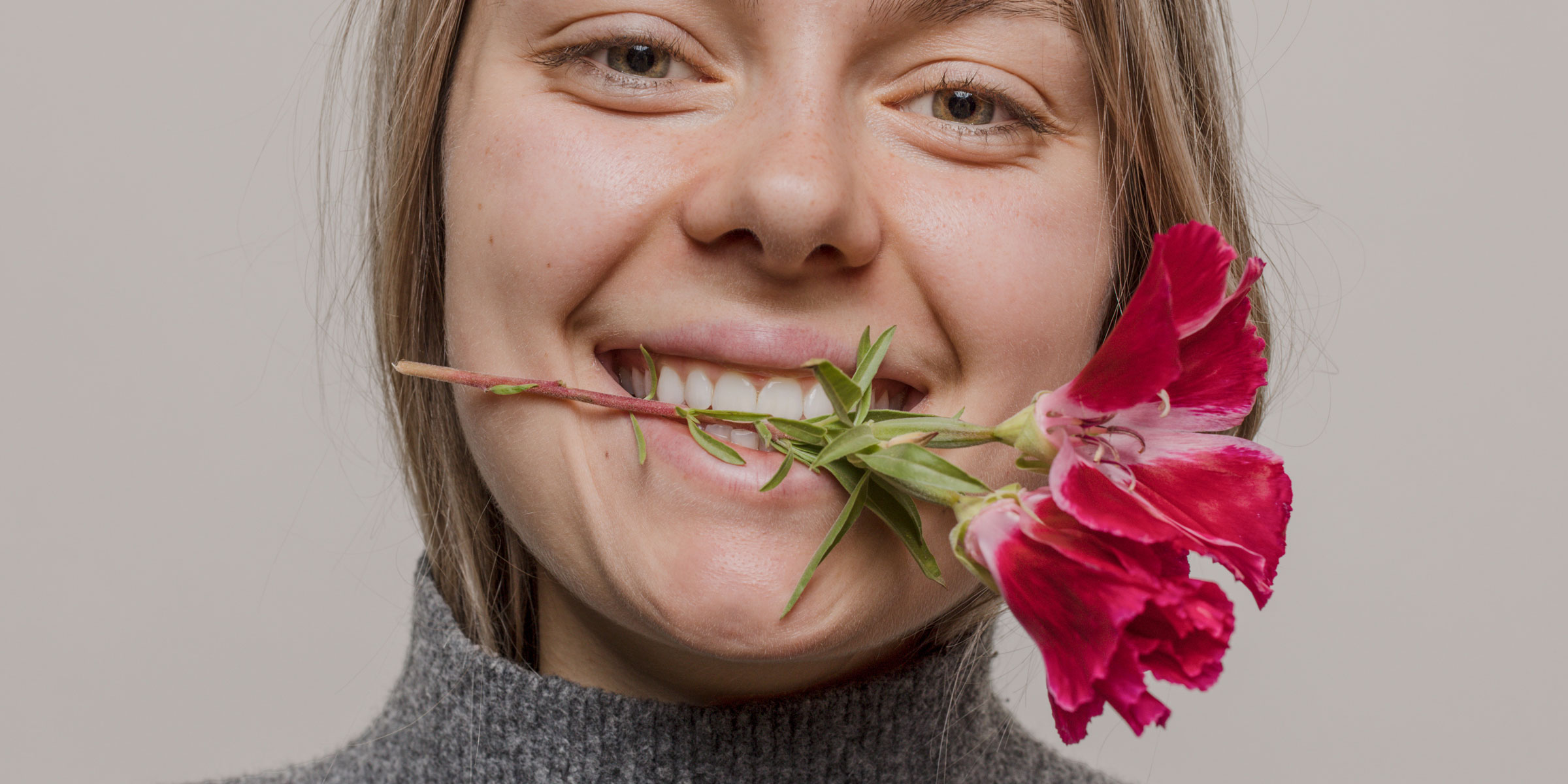 A woman's face with a red flower in her mouth