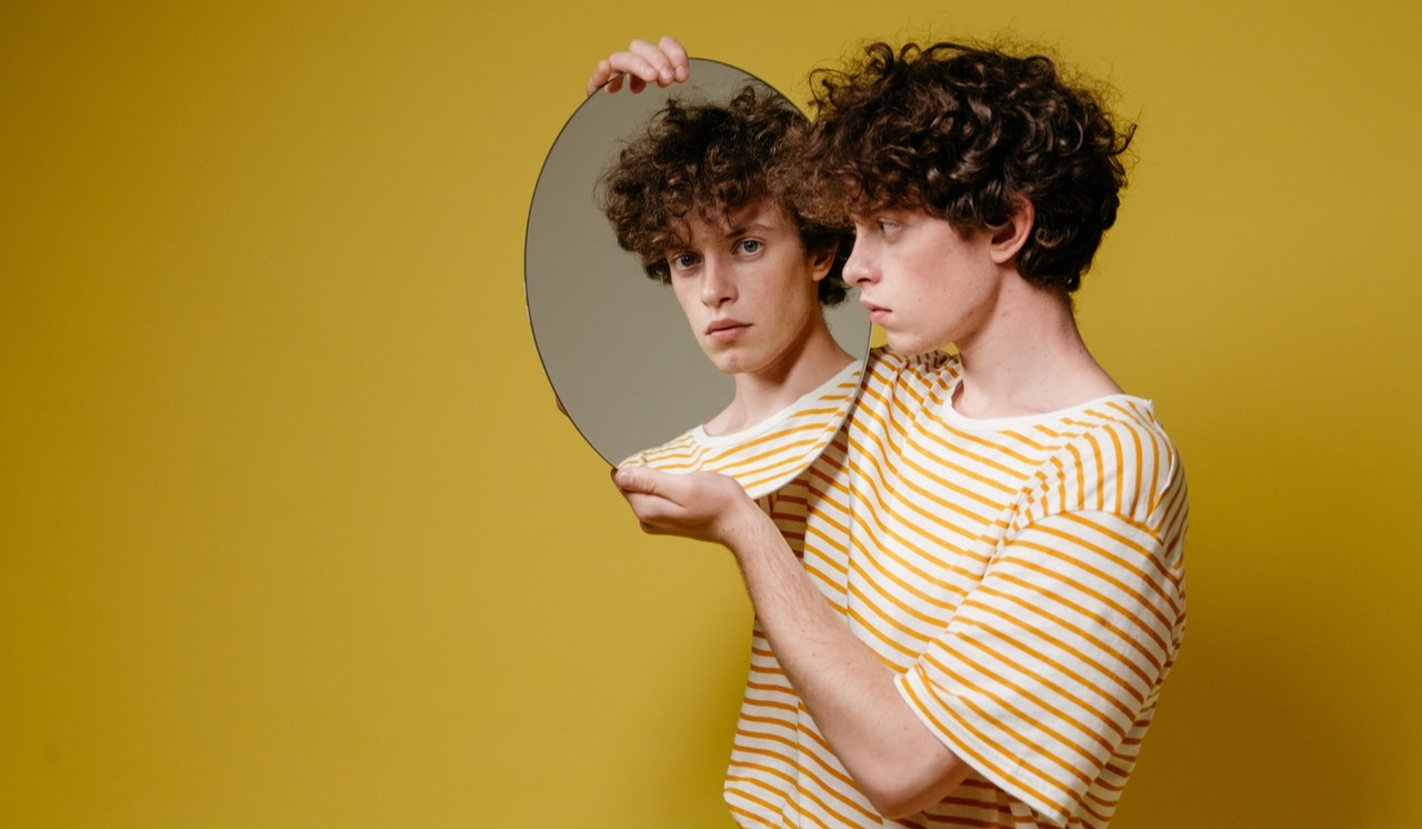 Man looking at his skin while holding a mirror