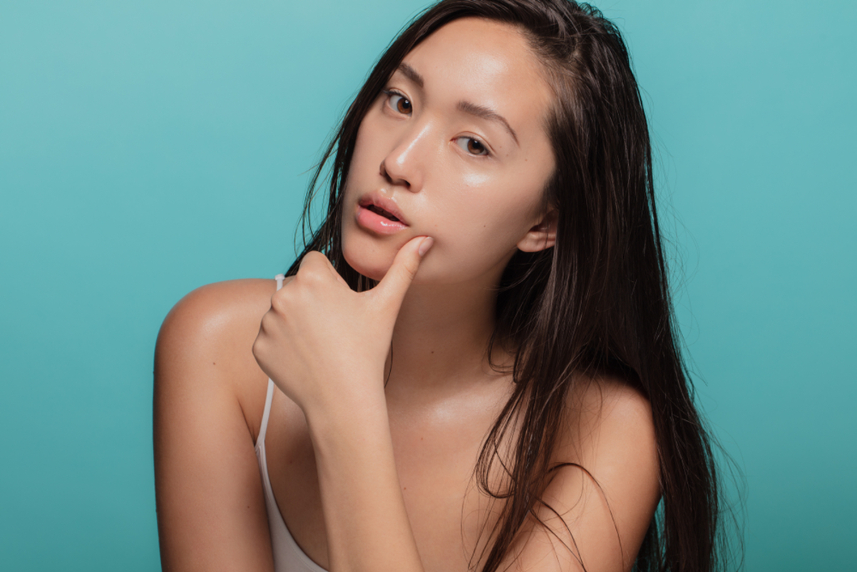 Young woman with glowing skin touching her face