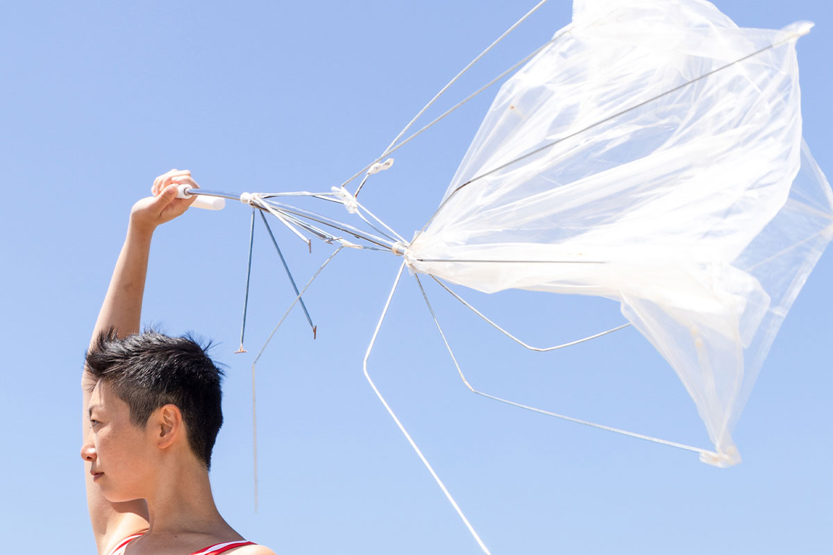 A person facing the sun while holding a broken umbrella above their head 