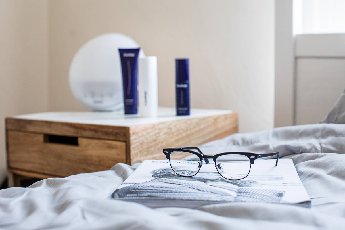Glasses resting on bed with Curology set on nightstand in background