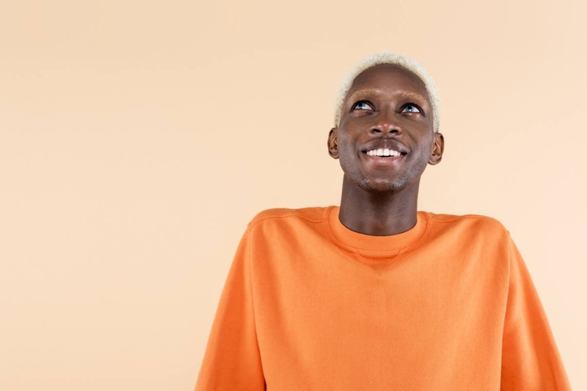 Afro man with bleached hair wearing orange shirt and smiling over orange background