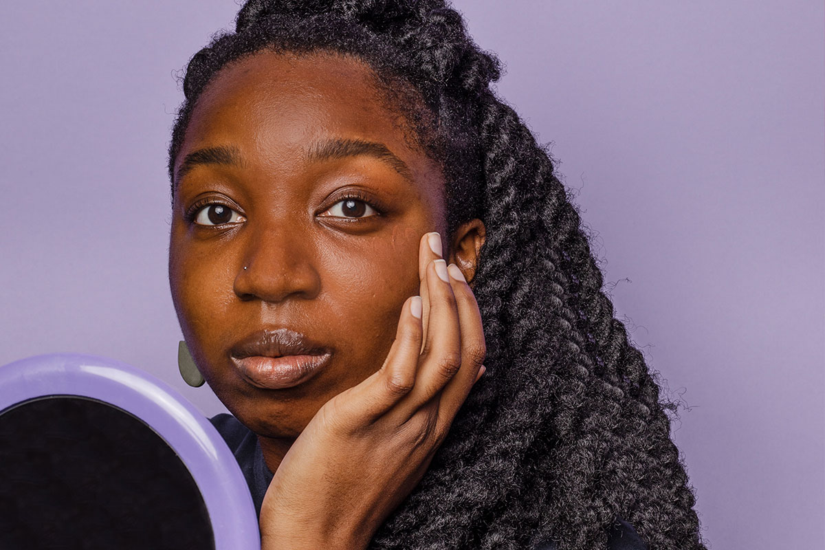 Portrait of a woman looking into the camera while holding a hand mirror and touching her face