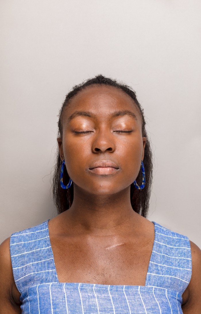 Woman with eyes closed and blue top with white stripes and blue earrings