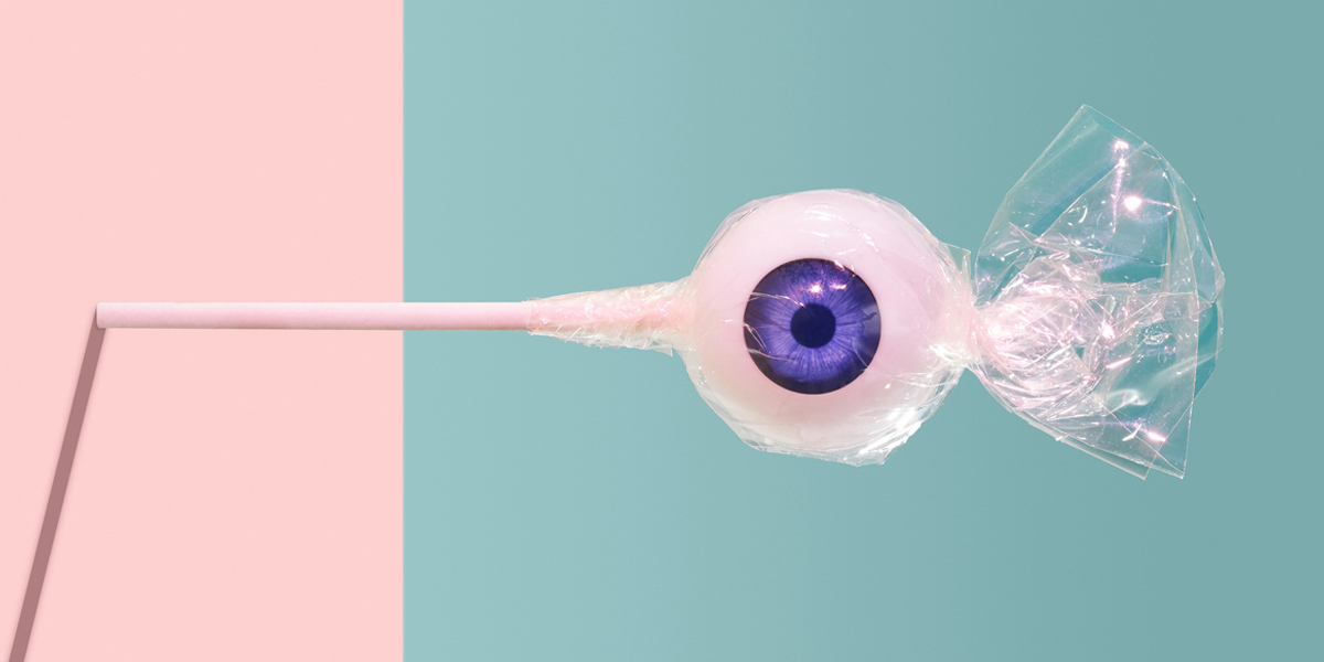 A wrapped lollipop resembling a blue eye against a pink and blue background.