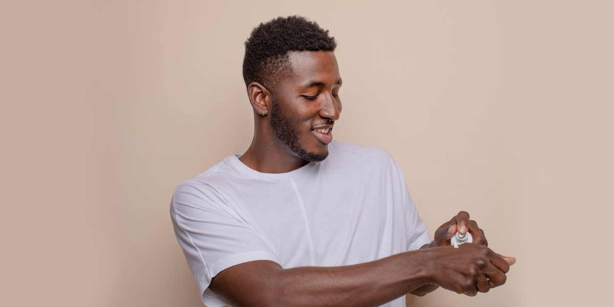 Man putting skincare cream on his hand with tan background