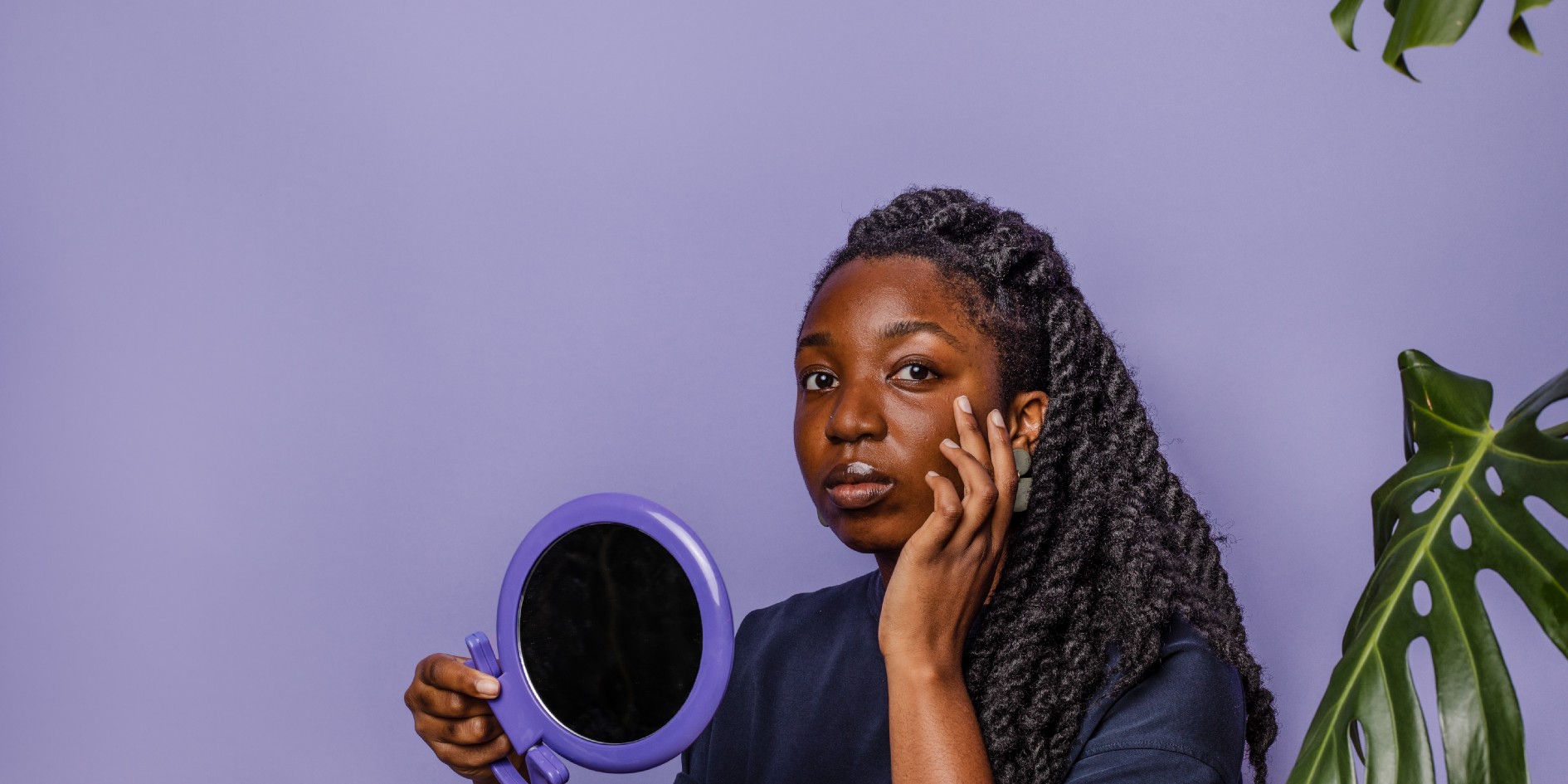 Woman holding mirror looking at camera with purple background 
