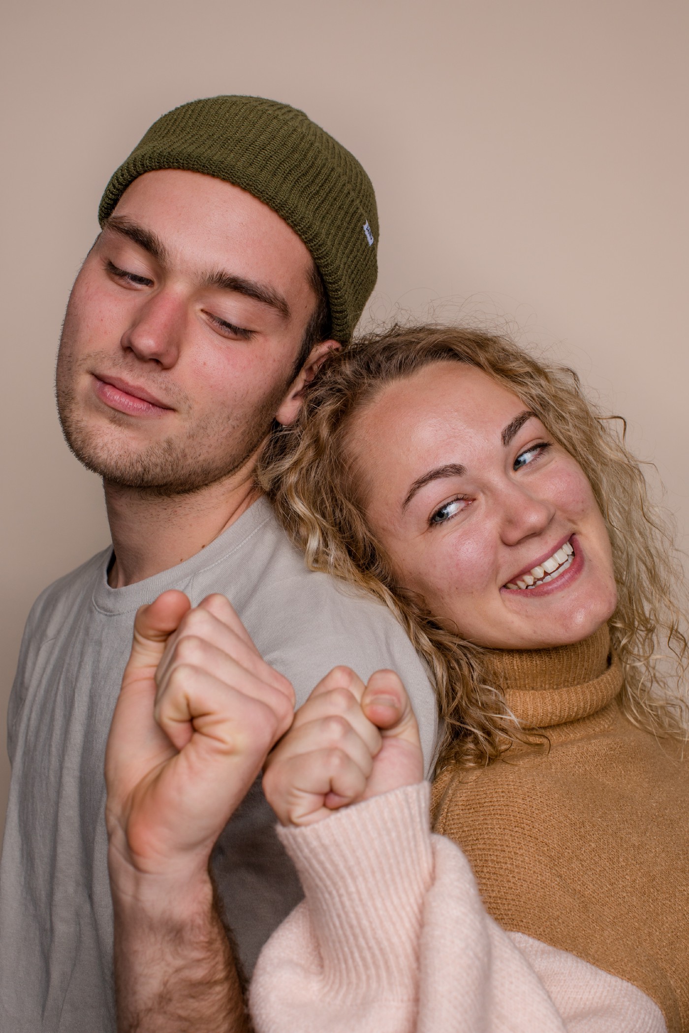 Man with green beanie and woman with curly hair leaning on eachother fist bumping