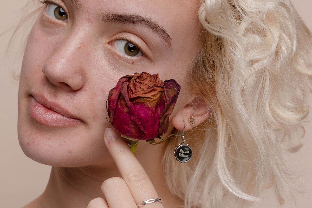 Woman holding dried rose next to cheek against a pale neutral background