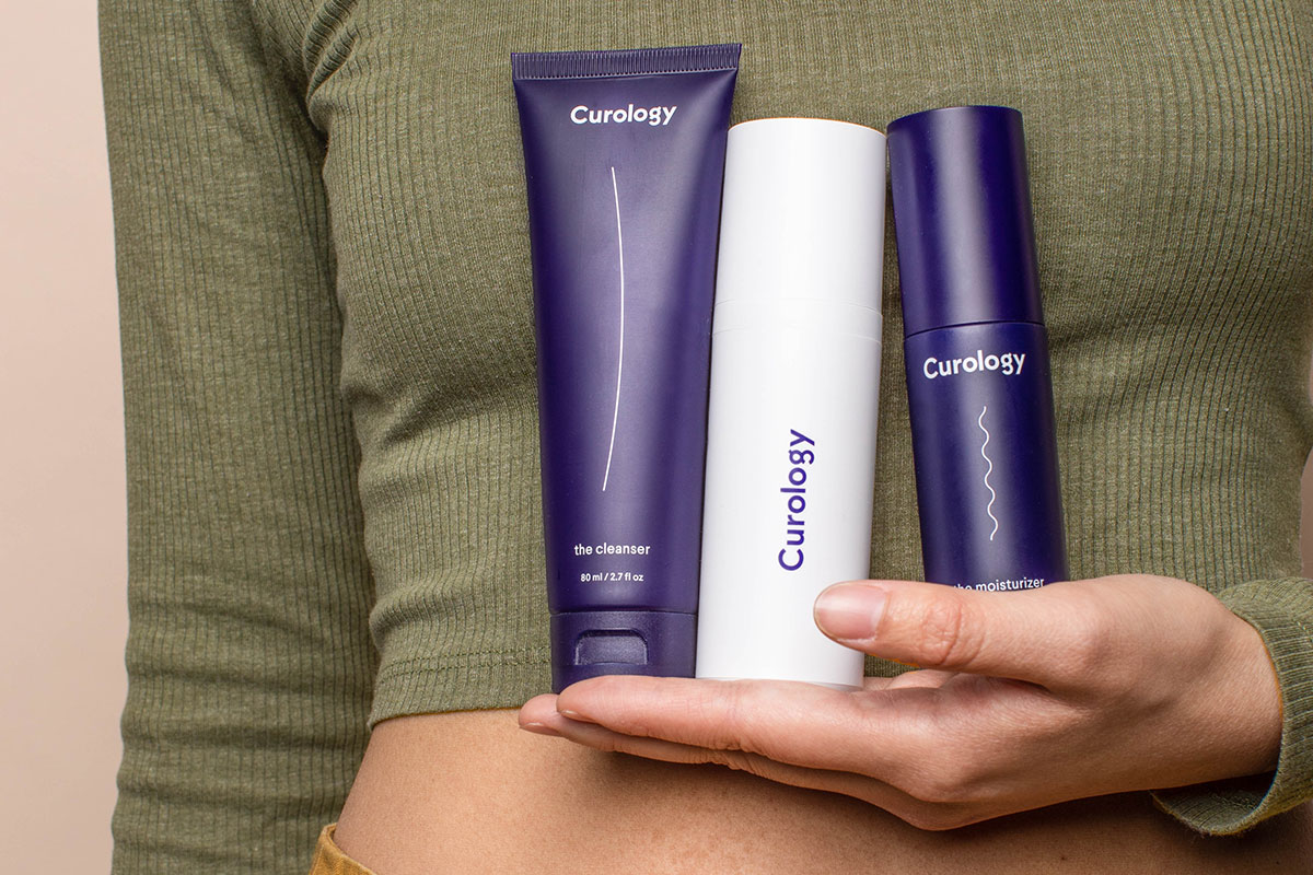 Person in green shirt holding Curology set with cleanser, moisturizer, and Curology bottle in front of chest