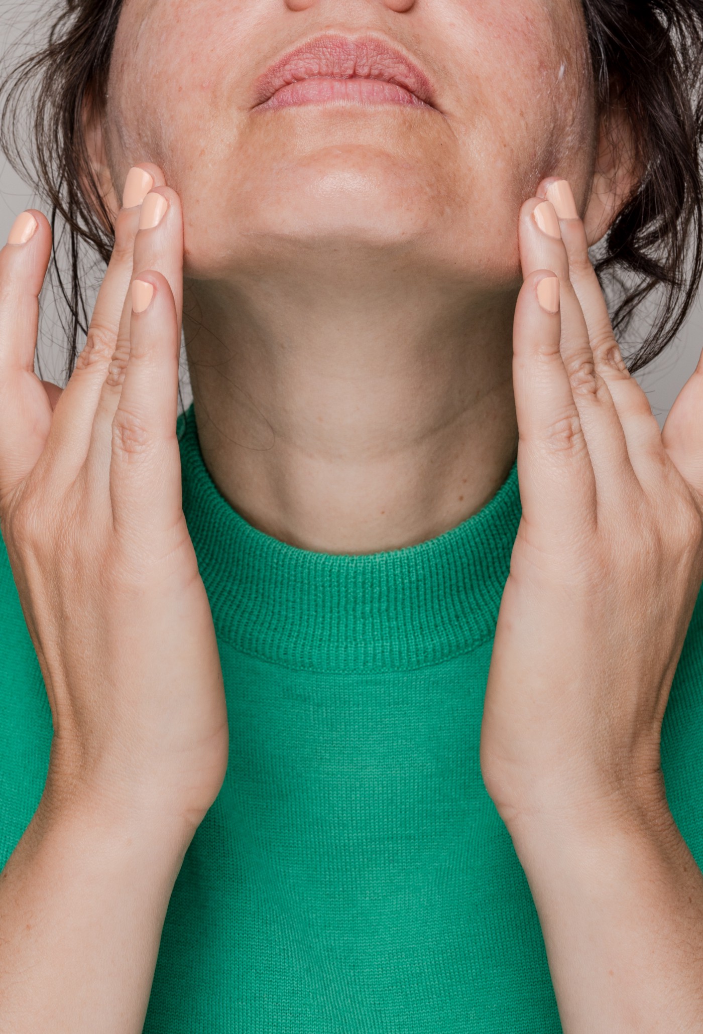 Woman with green top rubbing skincare cream on face