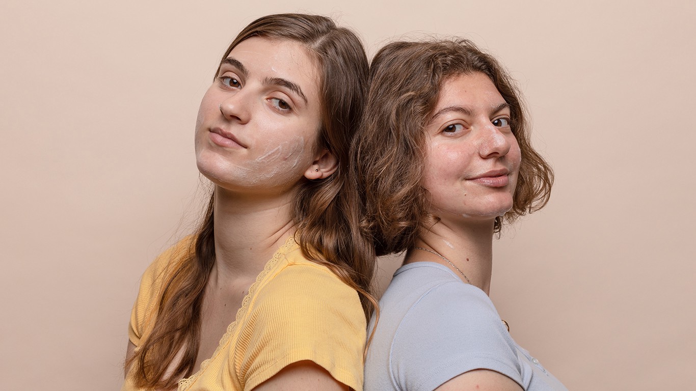 Two women back to back with skincare cream on their faces