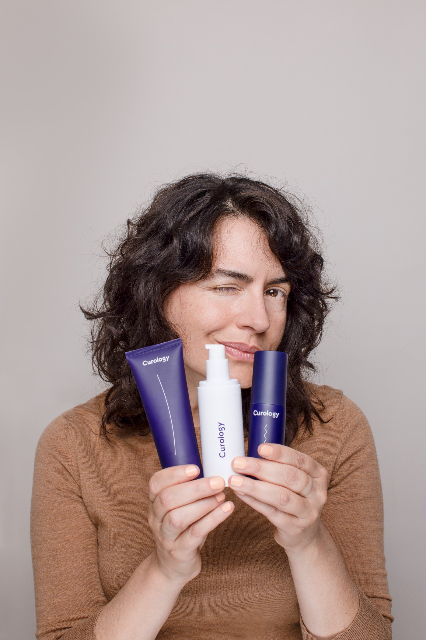 Woman with brown shirt holding curology bottles
