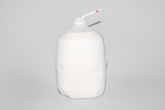 Full gallon jug of milk with a white and red straw against a gray neutral background