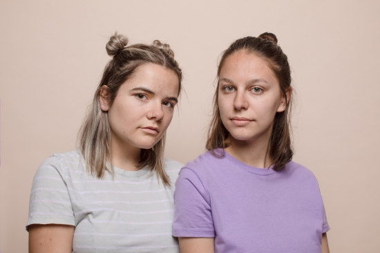 Women looking at camera with neutral background. Purple shirt and striped shirt