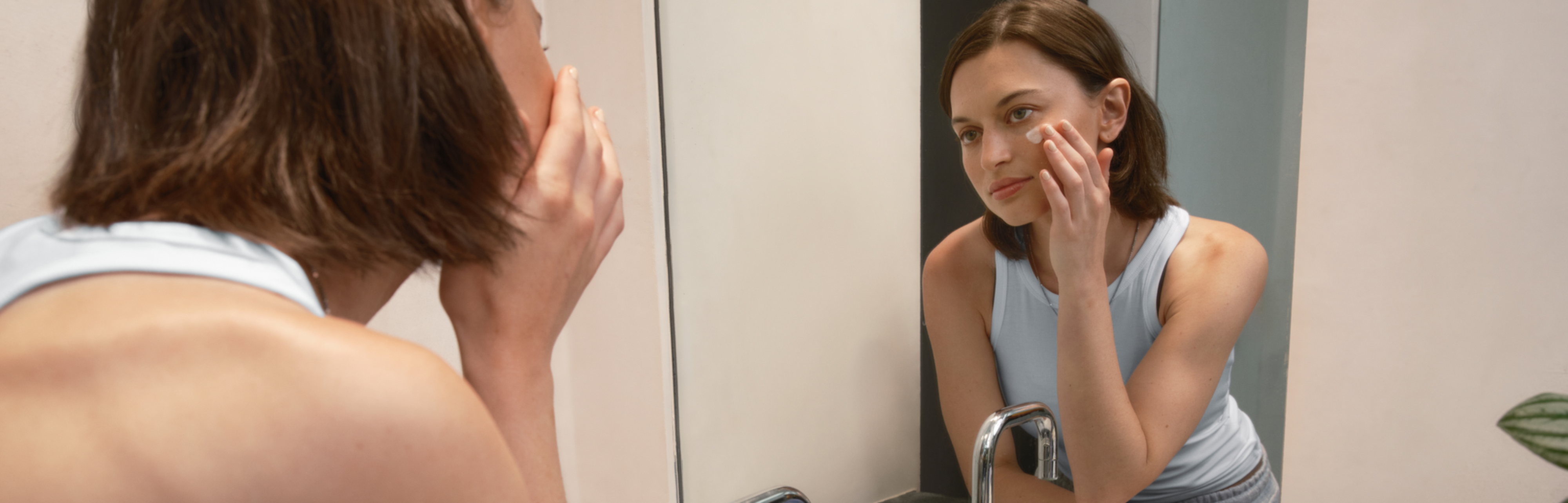 Young brunette with straight hair applying formula in bathroom mirror | Desktop